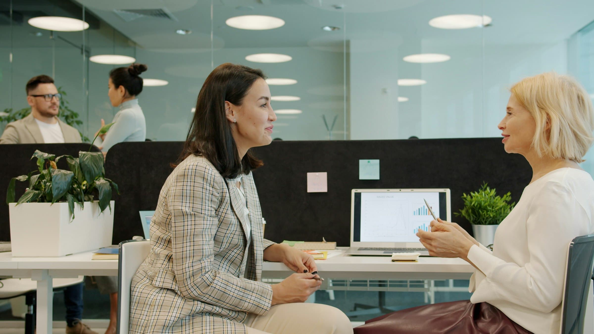 Two women in conversation across a desk in a bright office.
