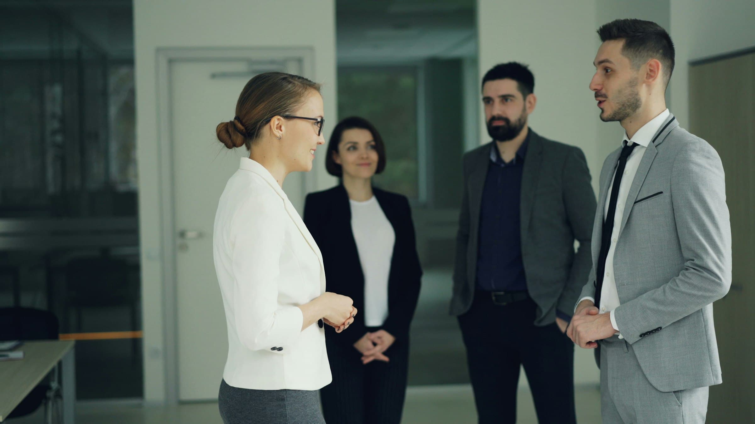 Four colleagues stand in a short meeting in an office corridor.